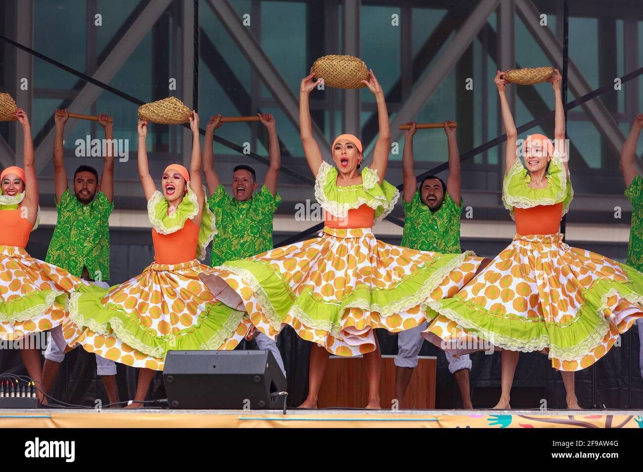 Eine Truppe von Tänzern aus Kolumbien in farbenfrohen grünen und orangen Outfits, die auf der Bühne mit Körben als Requisiten auftreten Stockfoto