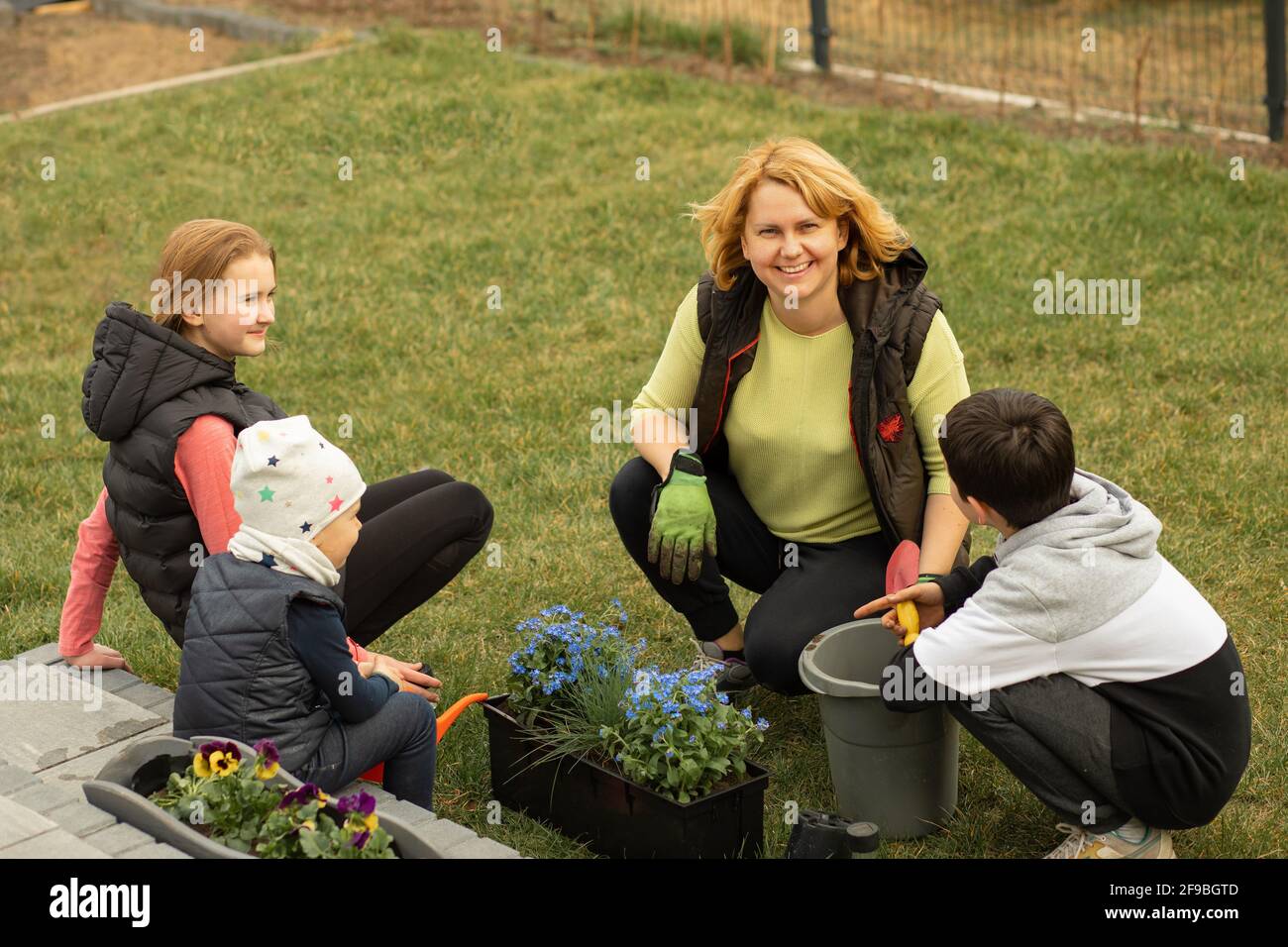 Mutter mit vielen Kindern pflanzt Blumen in Töpfen vor oder hinter dem Haus. Gerne verbringen Sie Zeit mit der Familie Stockfoto