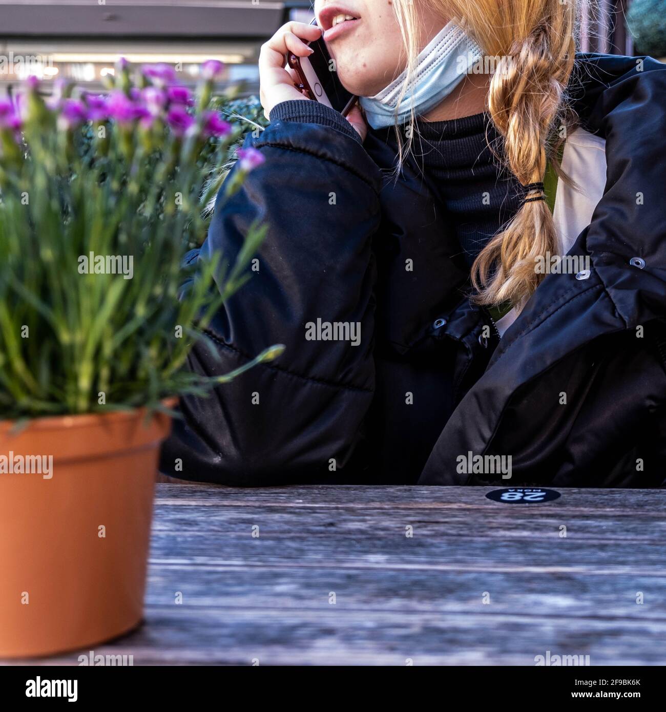 Epsom Surrey, London, Großbritannien, April 17 2021, Junge Frau, die allein an EINEM Tisch sitzt und ein Mobiltelefon mit EINER schützenden Gesichtsmaske trägt Stockfoto