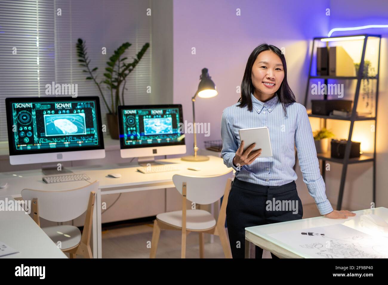 Porträt eines lächelnden, attraktiven asiatischen Autodesigners im abgestreiften Hemd Digitales Tablet in einem modernen Büro mit Computern halten Stockfoto