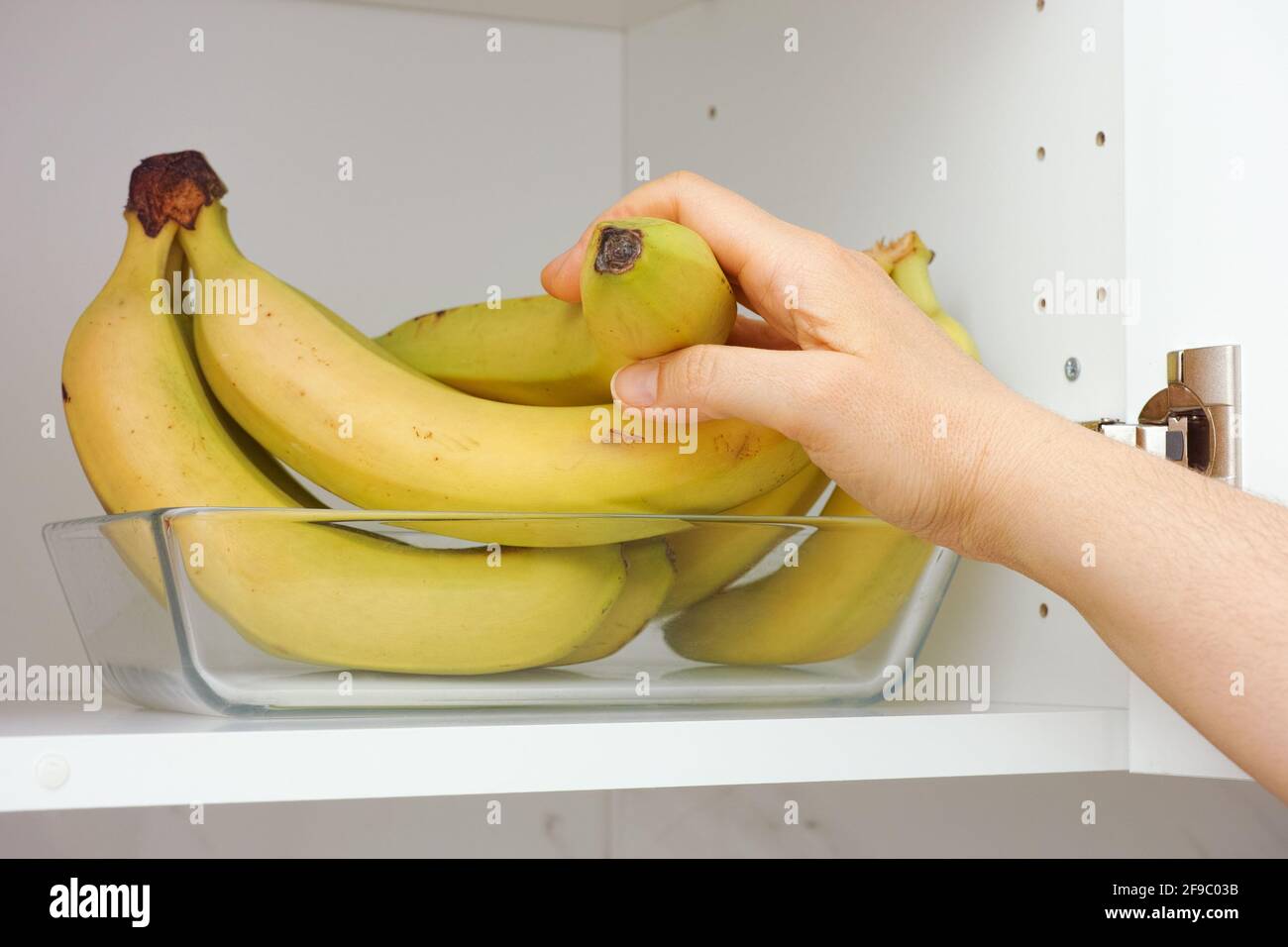 Eine Frau, die ein paar Bananen aus einem Glastablett in einem Küchenschrank nimmt. Nahaufnahme. Stockfoto