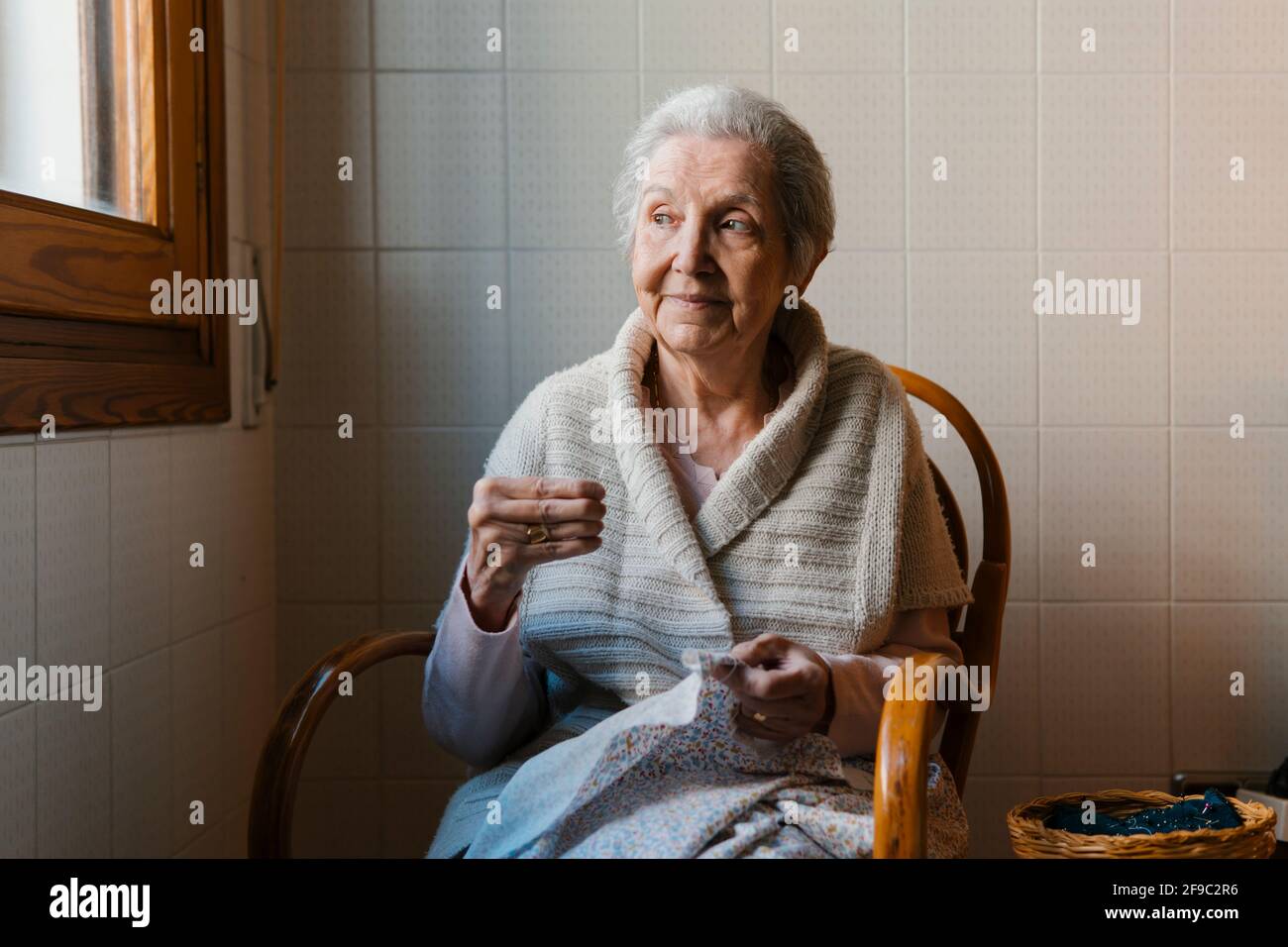 Großmutter näht mit Nadel und Faden, während sie den Blick aus Angezeigt Stockfoto