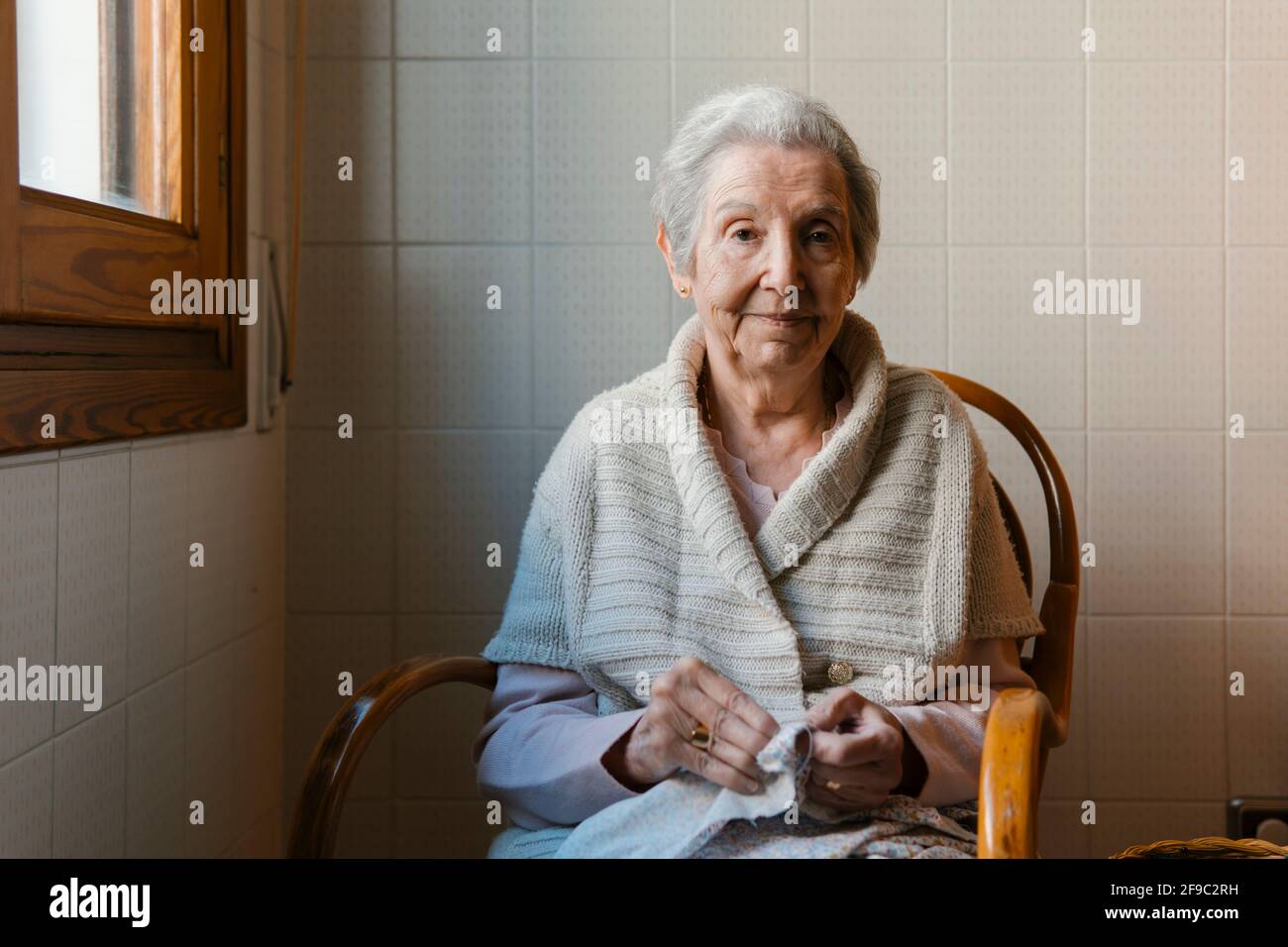 Großmutter näht mit Nadel und Faden, während sie die Kamera anschaut Stockfoto