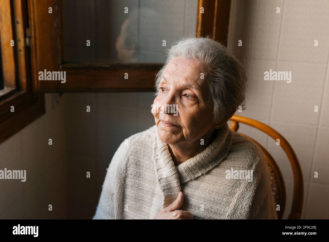 Porträt einer älteren Frau, die aus dem Fenster schaut Stockfoto