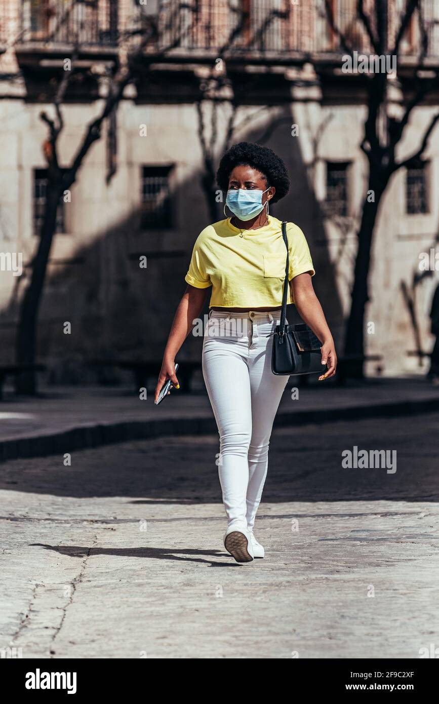 Schwarzes afro-amerikanisches Mädchen mit Gesichtsmaske, das eine Stadtstraße entlang läuft. Stockfoto
