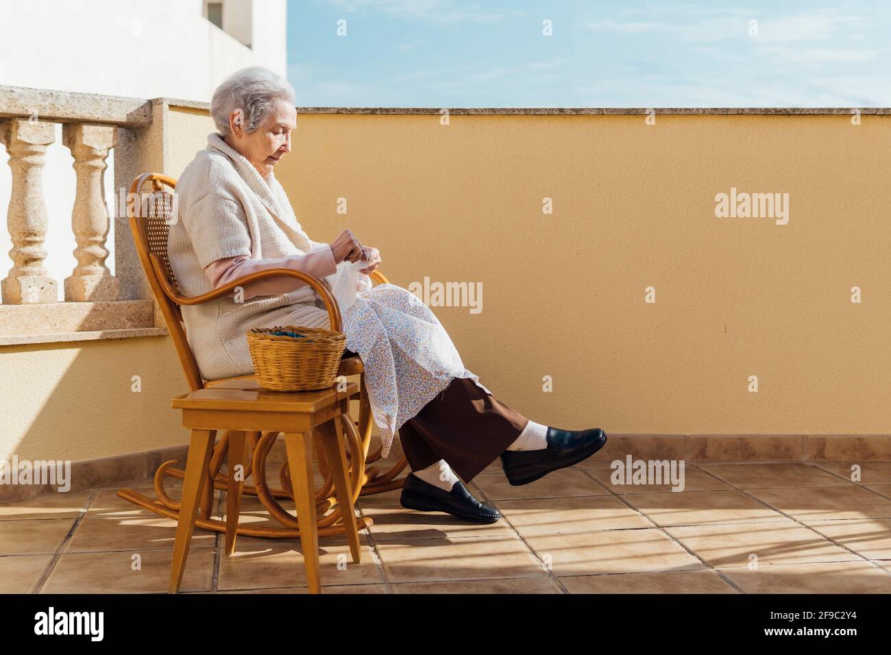 Ältere Frau, die auf der Außenterrasse mit Nadel und Faden Nähte Stockfoto