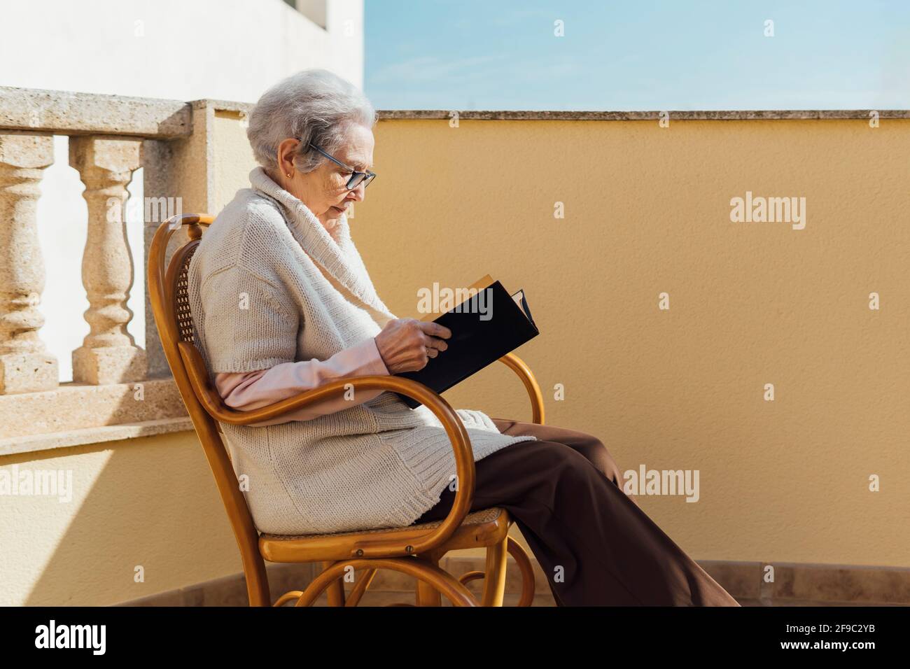 Ältere Frau liest auf einer sonnigen Terrasse im Freien Stockfoto