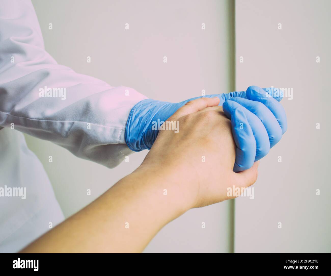 Die Hand einer Frau, die die Hand eines Arztes mit einem blauen Handschuh hält Stockfoto