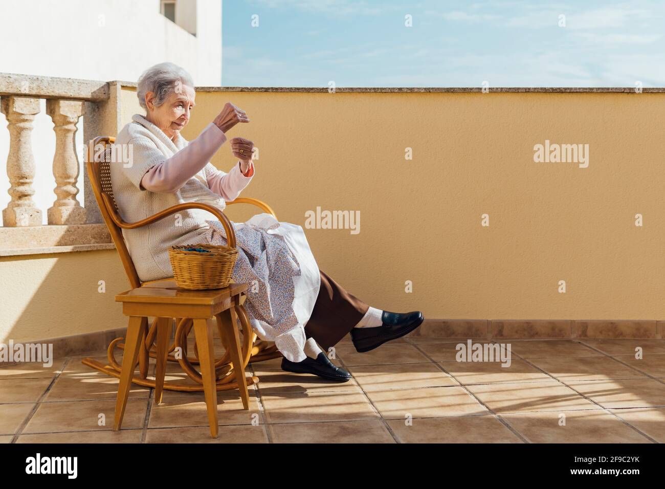 Ältere Frau, die auf der Außenterrasse mit Nadel und Faden Nähte Stockfoto
