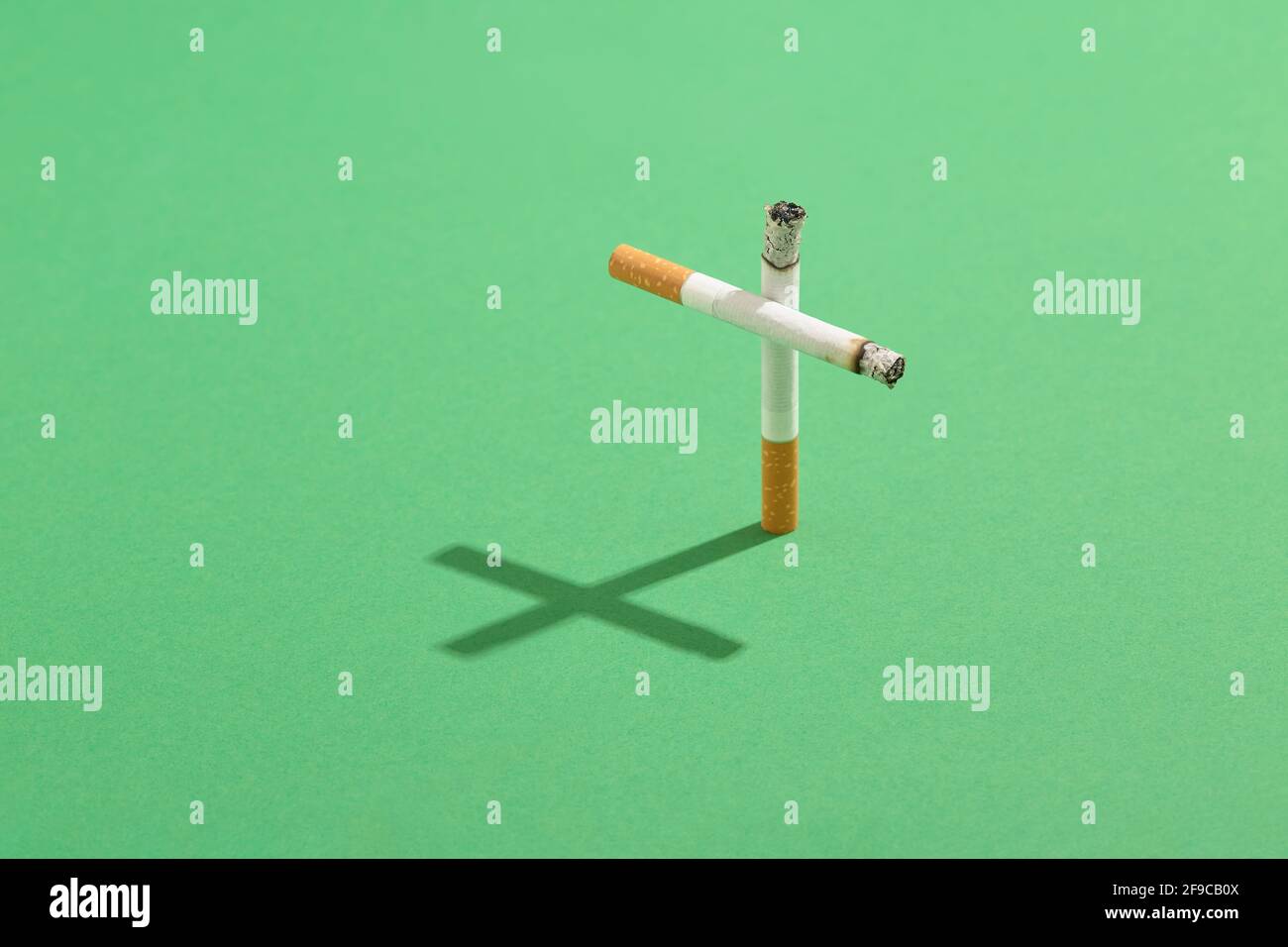 Rauchen tötet Konzept mit Zigaretten als Grabkreuz mit dem Kreuzschatten auf grünem Friedhof Rasen. Stockfoto
