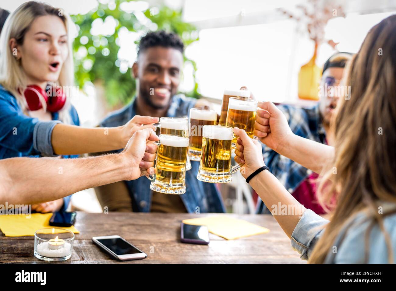 Fröhliche, multirassische Freunde, die in der Brauerei-Bar Bier trinken und toasten - Freundschaftskonzept mit jungen Leuten, die Spaß zusammen haben Cooles Pub-Restaurant Stockfoto