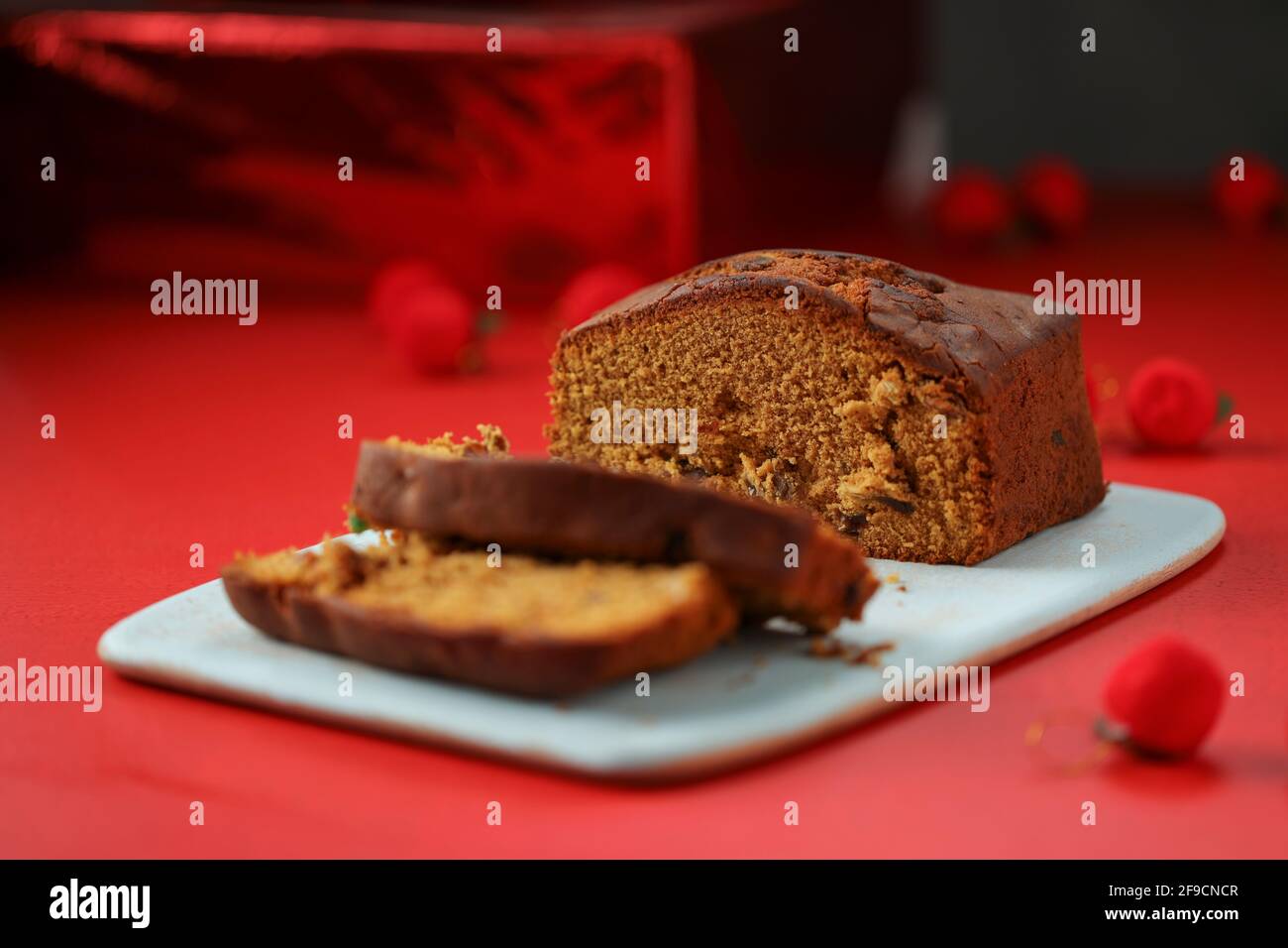 Pflaumenkuchen, hausgemachter leckerer Christmus-Kuchen mit Rosinen, Cashewnüssen und getrockneten Früchten, die in Scheiben geschnitten und mit rotem Backgro an Bord platziert werden Stockfoto