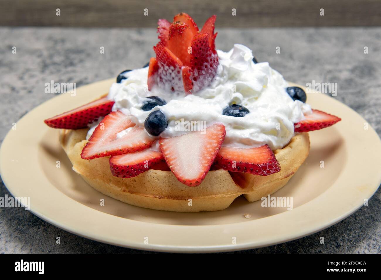 Dekorative Erdbeerscheiben und Skulpturen, die mit Heidelbeeren und Schlagsahne auf herzhafte Waffeln gestapelt sind. Stockfoto