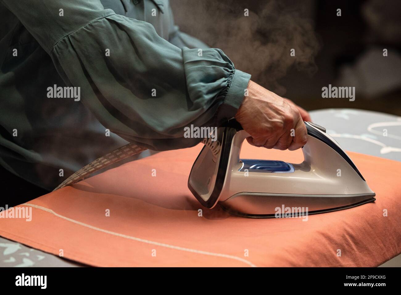 Ältere Frau isoliert auf weißem Hintergrund, Kleidung bügeln Stockfoto