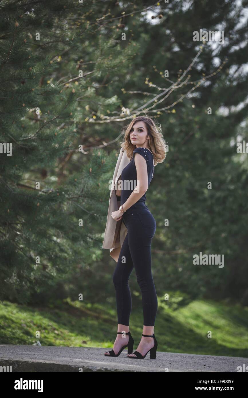 Schlanke junge Dame in schwarzer Kleidung und Schuhen mit hohem Absatz Posiert im natürlichen Hintergrund Stockfoto