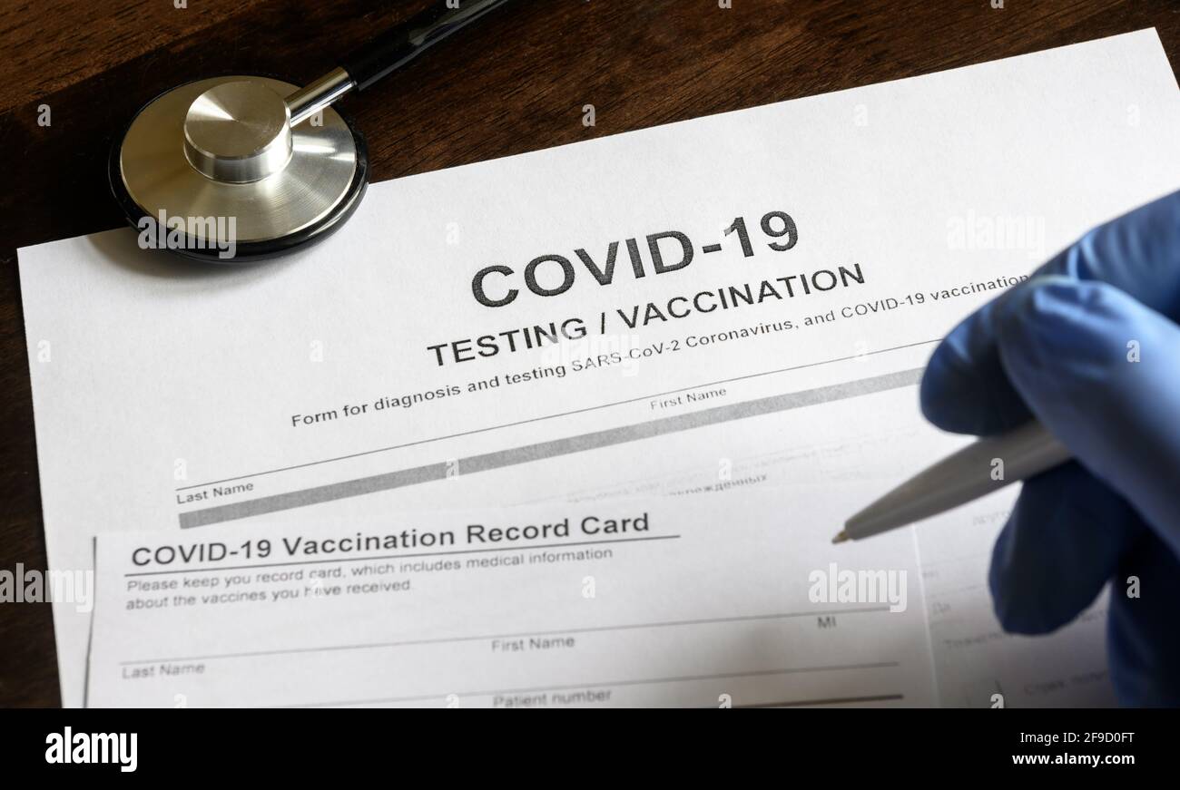 COVID-19 Test- und Impfformulare am Schreibtisch, Arzt nimmt einen Eintrag in Coronavirus-Impfpass, medizinisches Dokument in der Klinik. Konzept von coron Stockfoto