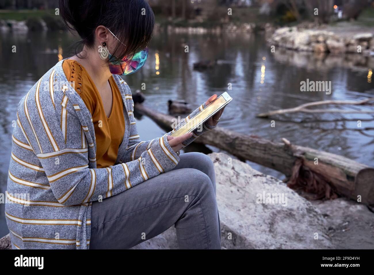 Eine Frau, die bei Einbruch der Dunkelheit am Ufer eines Sees sitzt und eine schöne Zeit mit der Tablette hat. Konzept von Ruhe und Freizeit. Stockfoto