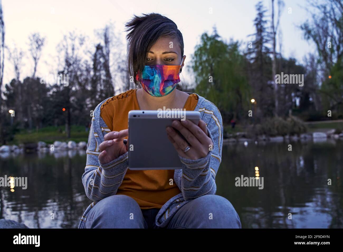 Eine Frau, die in der Abenddämmerung draußen mit einem See hinter sich auf dem Tablet liest. Konzept von Ruhe und Freizeit. Stockfoto