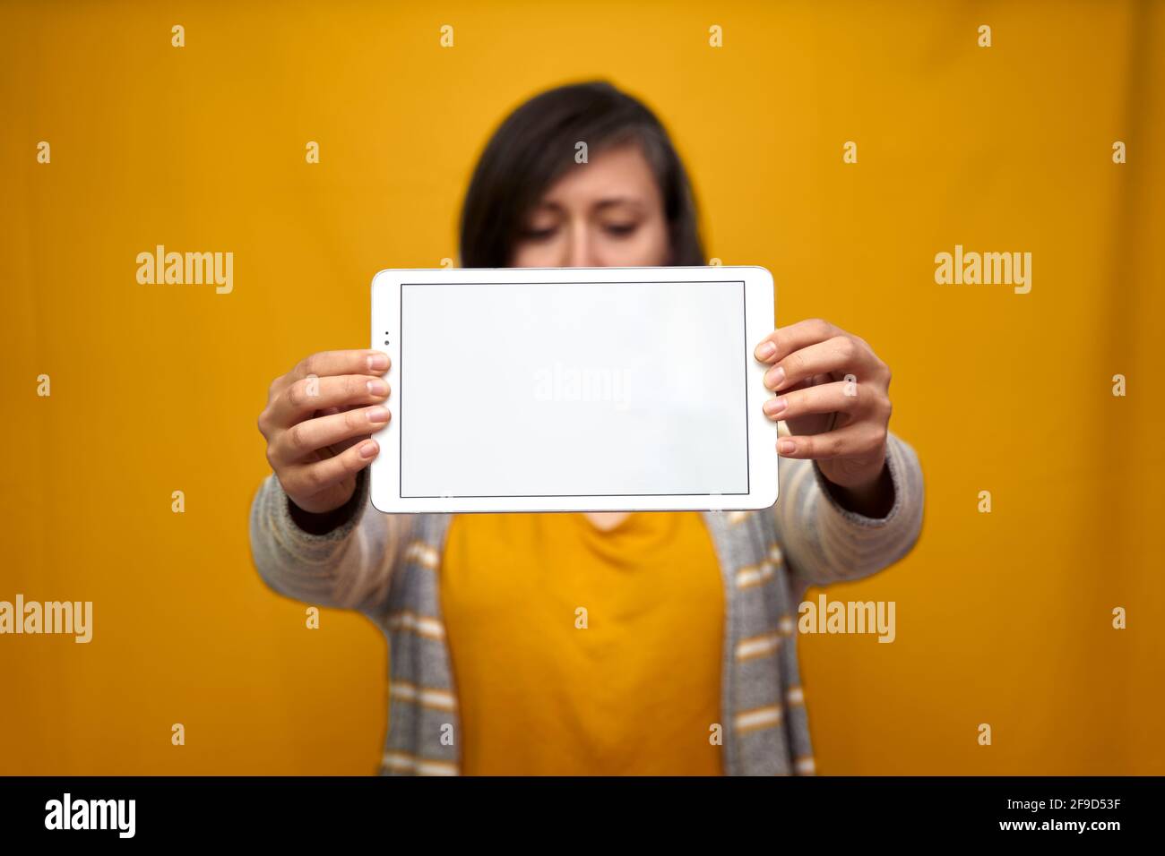 Eine Frau, die nicht fokussiert war und einen fokussierten Tablet-pc vor ihrem Gesicht auf goldgelbem Hintergrund hielt. Konzept der Technologie, Gadgets. Stockfoto
