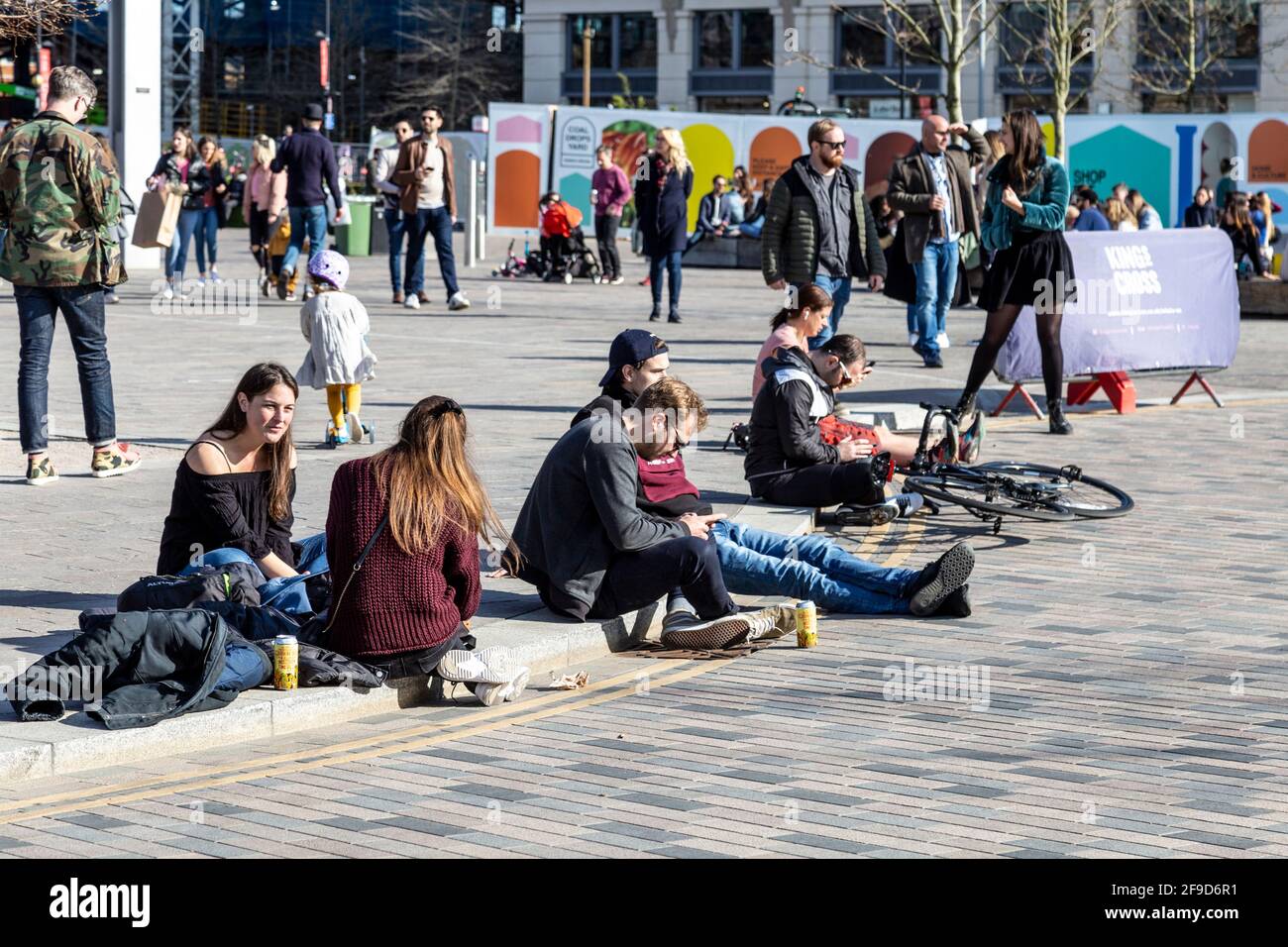 17. April 2021 - London, Großbritannien, Menschen, die auf dem Bürgersteig sitzen und am sonnigen Wochenende auf dem Kings Cross Granary Square reden, nachdem die Sperrung der Coronavirus-Pandemie gelockert wurde Stockfoto