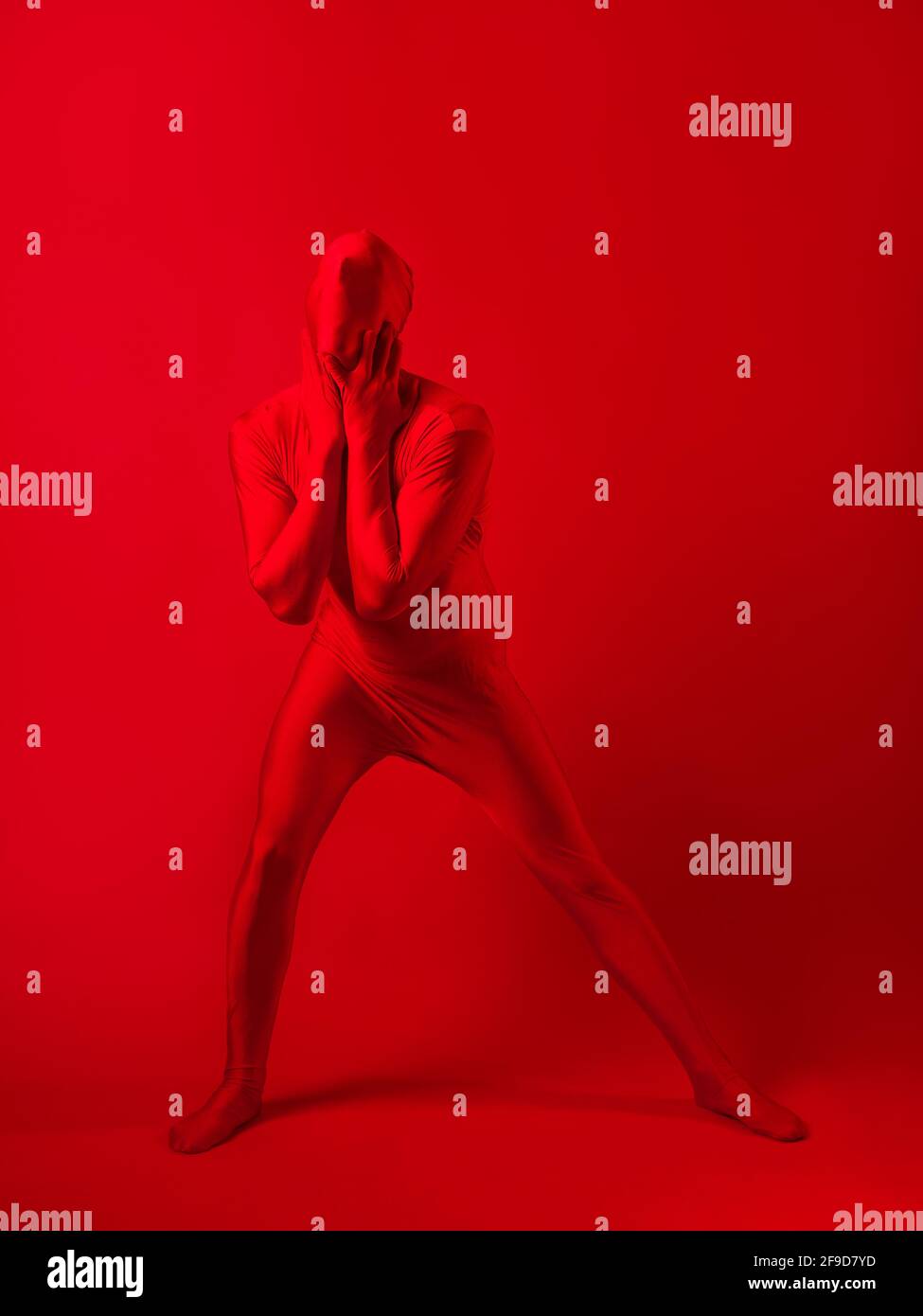 Verrückter roter Mann auf rotem Hintergrund. Figur in einem Trikot, das den ganzen Körper und Gesicht bedeckt und versucht, sich mit dem Hintergrund zu vermischen. Stockfoto