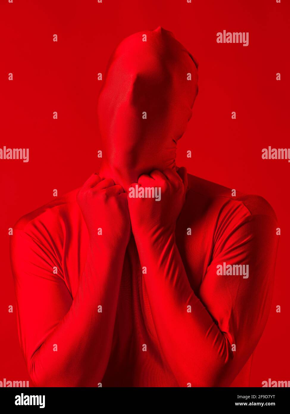 Verrückter roter Mann auf rotem Hintergrund. Figur in einem Trikot, das den ganzen Körper und Gesicht bedeckt und versucht, sich mit dem Hintergrund zu vermischen. Stockfoto