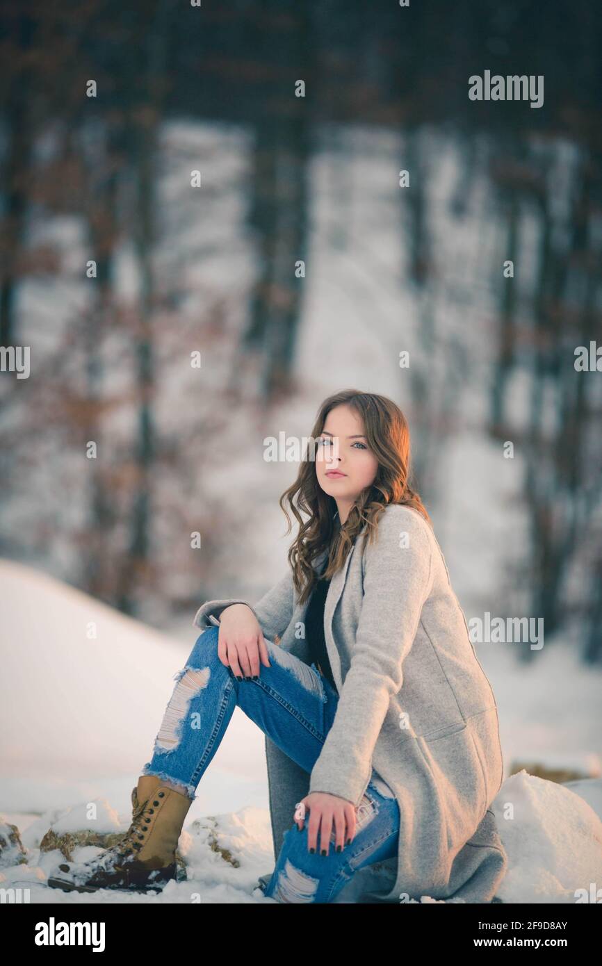 Schöne bosnisch kaukasische Frau in Mantel und Stiefel Blick auf Die Kamera mit ernsthafteren Gesicht im Schnee Stockfoto