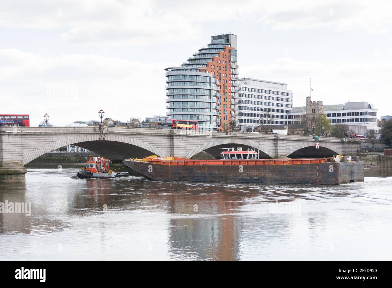 Ein Schleppboot und ein großer Lastkahn fahren unter der Putney Bridge mit dem Apartmentblock Putney Wharf Tower im Hintergrund, London, SW15, England, Großbritannien Stockfoto