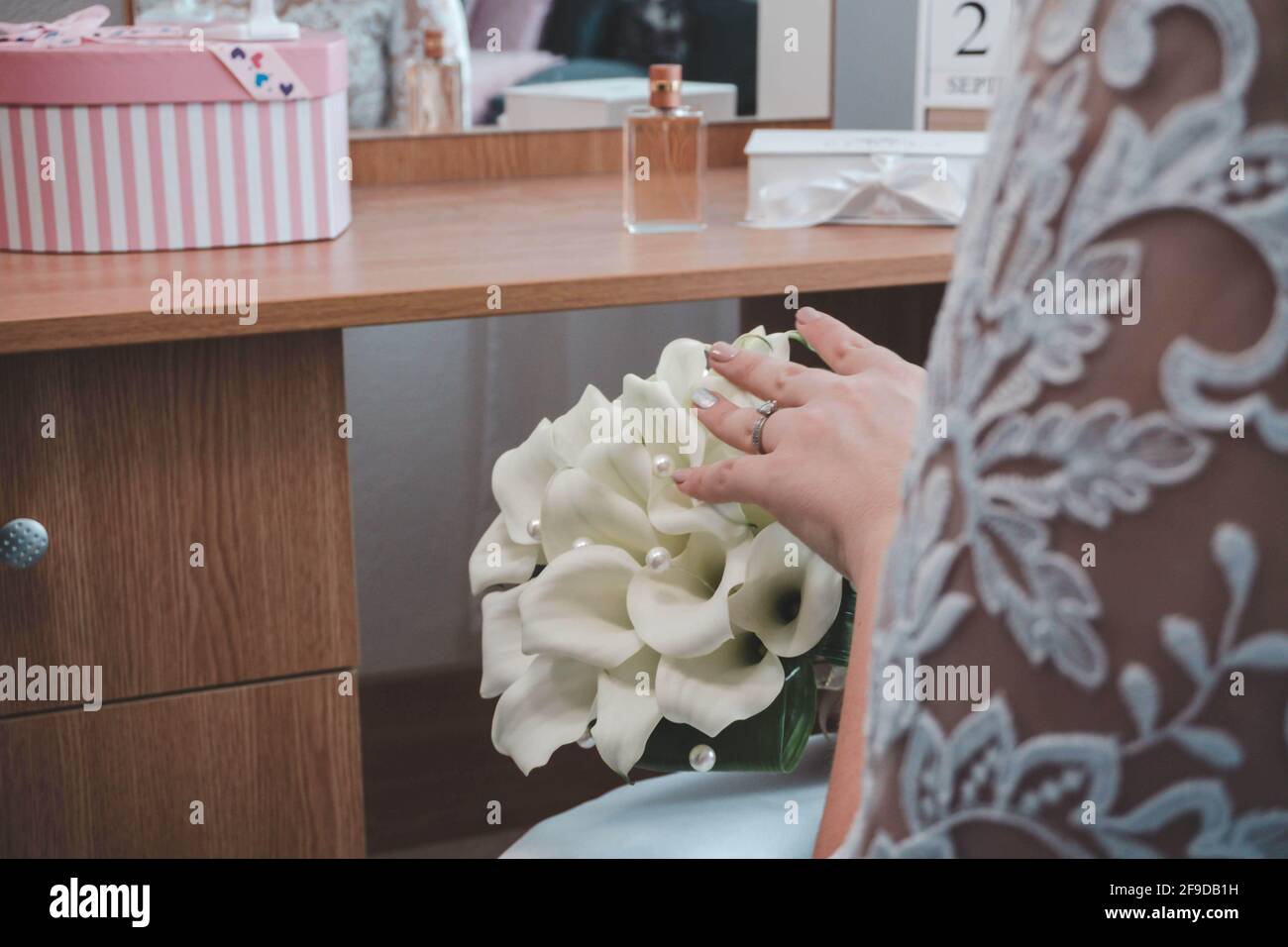 Nahaufnahme der Hand einer Braut auf einem weißen Brautkleid Blumenstrauß, während sie in ihrem Zimmer sitzt Stockfoto
