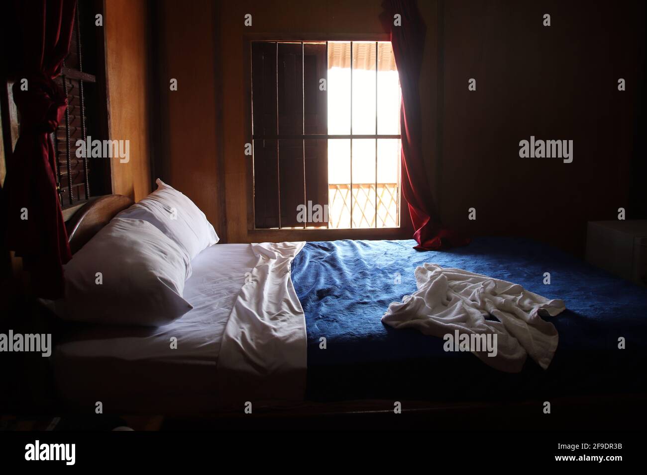 Ein ländliches kleines Schlafzimmer mit einem blau bedeckten Bett Bettwäsche und ein Fenster Stockfoto