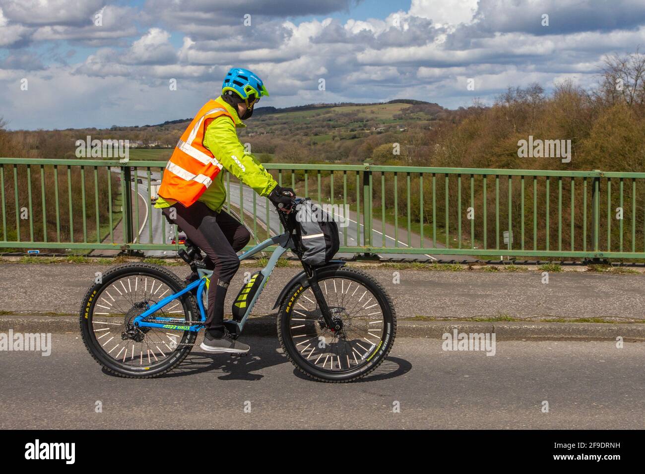 Männlicher Radfahrer, der auf einer Landstraße über die Autobahnbrücke im ländlichen Lancashire, Großbritannien, mit einem batteriebetriebenen Fahrrad unterwegs ist Stockfoto