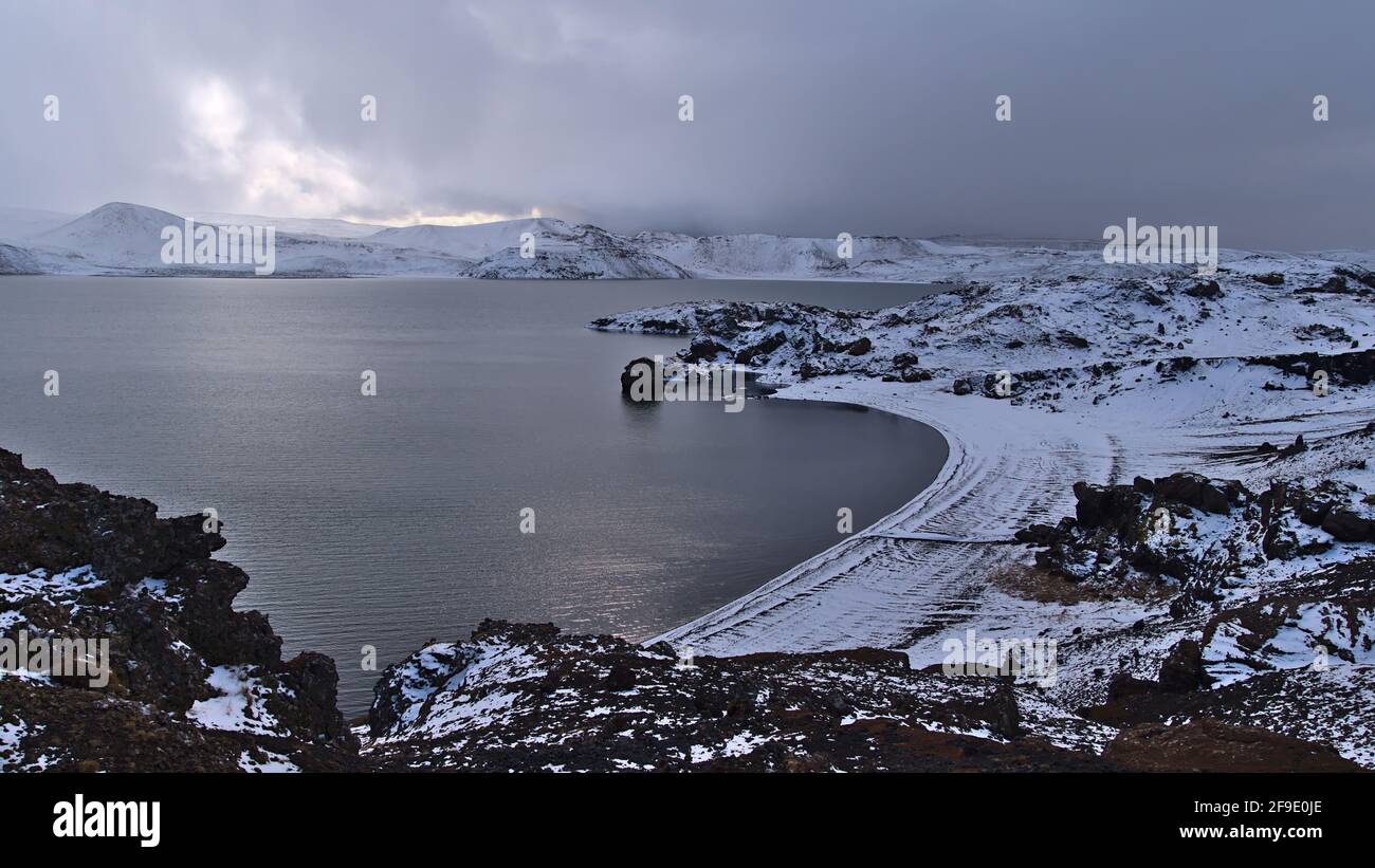 Atemberaubender Blick über den felsigen, schneebedeckten Strand am Ufer des Kleifarvatn-Sees in Krýsuvík, Halbinsel Reykjanes, Island in der Wintersaison mit Bergen. Stockfoto