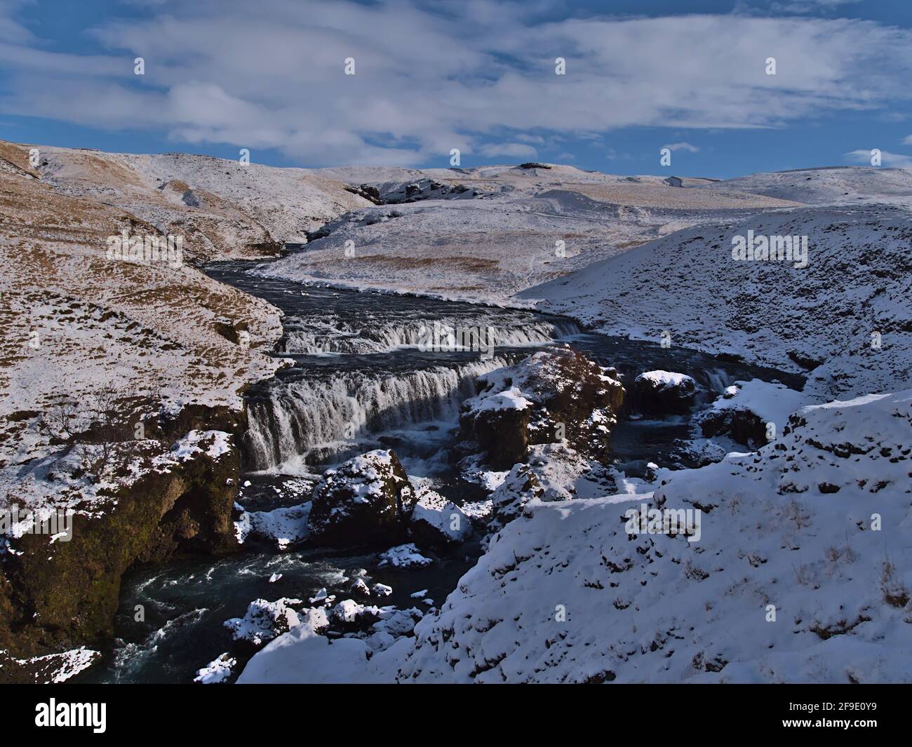 Schöner Blick auf die Wasserkaskaden des Flusses Skógá in der Nähe des Fimmvörðuháls-Weges in einer felsigen Schlucht, umgeben von schneebedeckten Wiesen am sonnigen Wintertag. Stockfoto