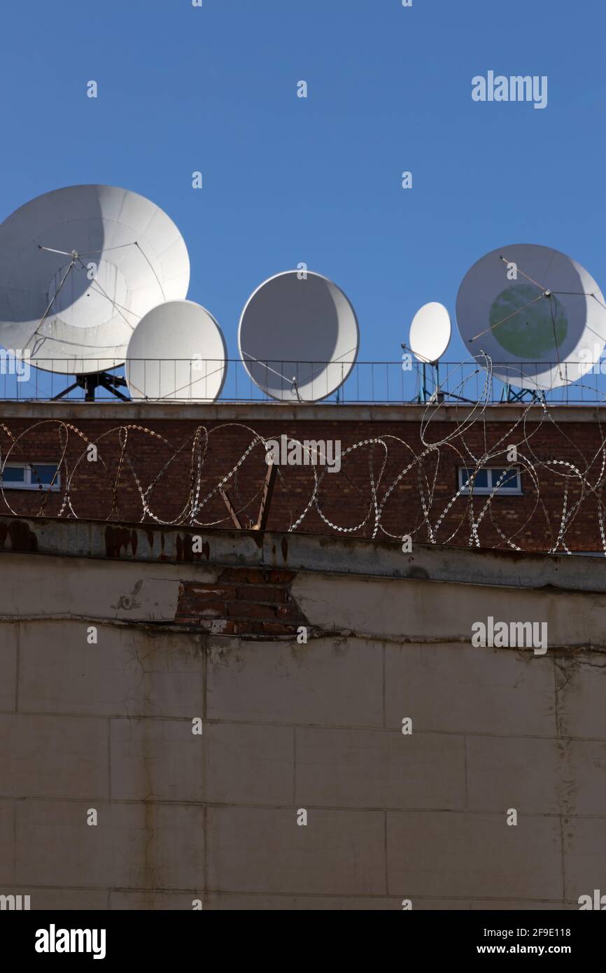 Selektive Fokussierung auf einen Zaun mit einem scharfen Stachelband Im Hintergrund Satellitenantennen und blauer Himmel Vertikale Ausrichtung Stockfoto