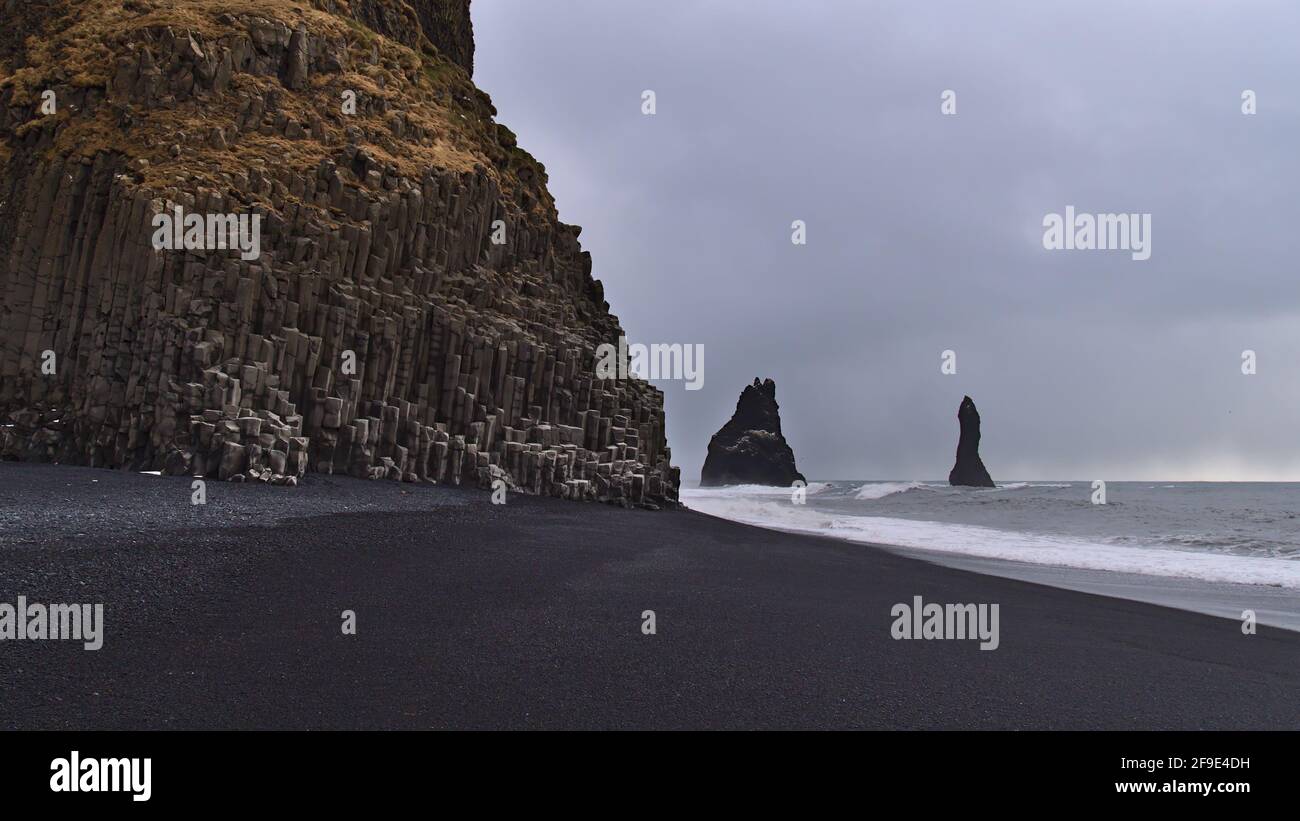 Blick auf den berühmten Strand Reynisfjara an der Südküste Islands mit schwarzen Kieselsteinen und Basaltsteinformationen am bewölkten Wintertag mit Wellen. Stockfoto