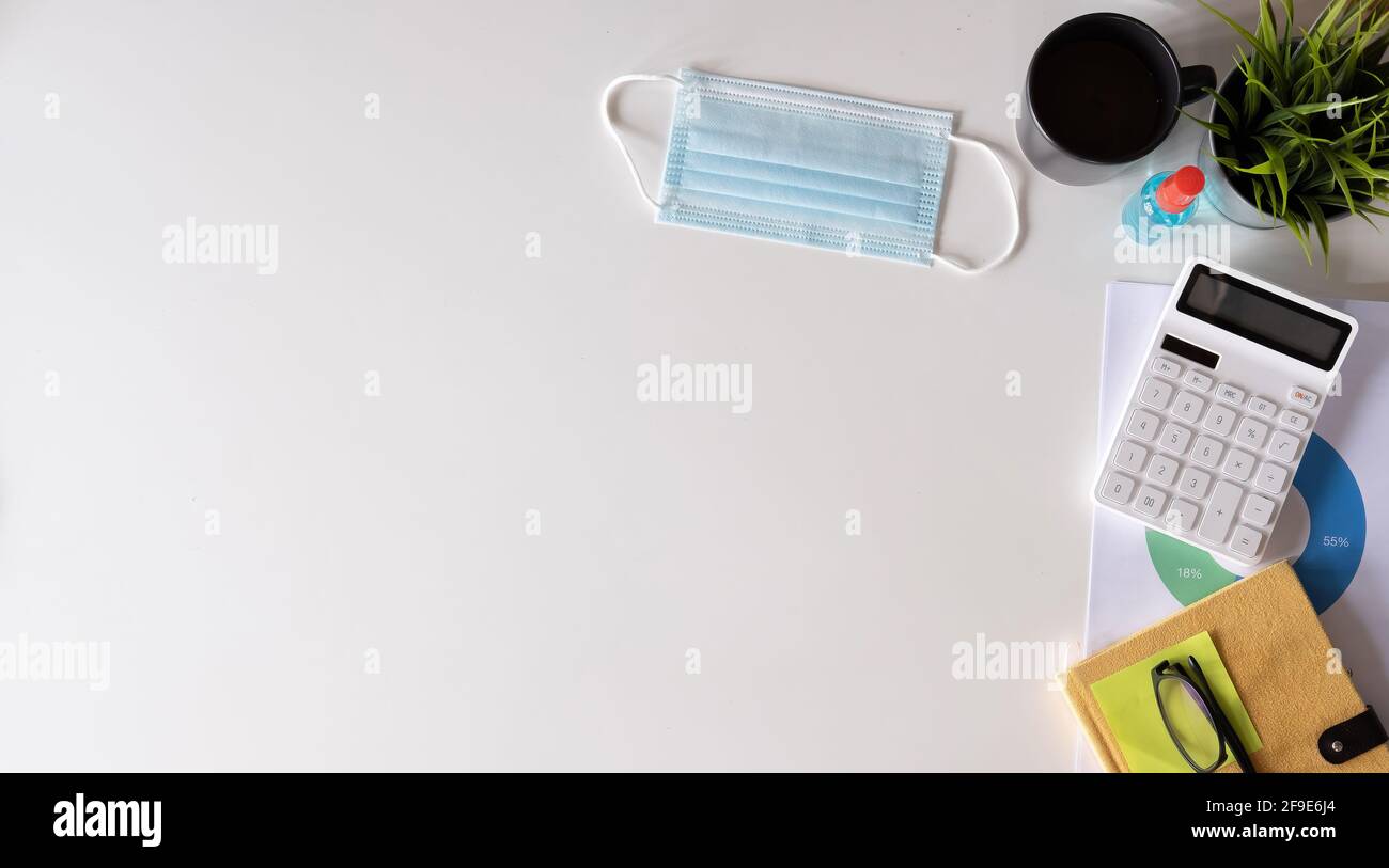 Weißer Schreibtisch mit chirurgischer Gesichtsmaske und Desinfektionsflasche oder Alkoholgel mit Kalkulator auf weißem Hintergrund isoliert, Arbeit von zu Hause und Stockfoto