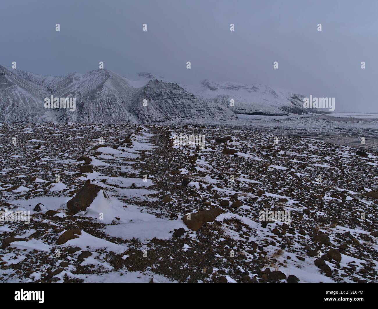 Schneebedeckter Felsenwanderweg im Skaftafell Nationalpark mit schöner Aussicht auf die schroffen Berge von Öræfajökull und die karge Landschaft. Stockfoto
