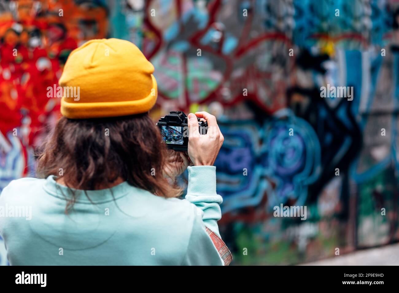 Rückansicht des anonymen Hipster-Männchens in gestrickter Hutnahme Foto der Graffiti-Wand auf der Kamera in der Stadt Stockfoto