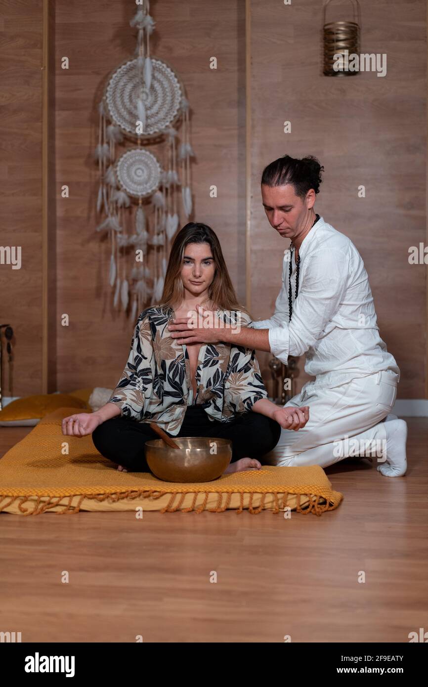 Zen-Lehrer in weißer Kleidung berühren Brust des Weibchens mit Gekreuzte  Beine während des Yoga-Trainings in der Nähe von Bowl gong Stockfotografie  - Alamy