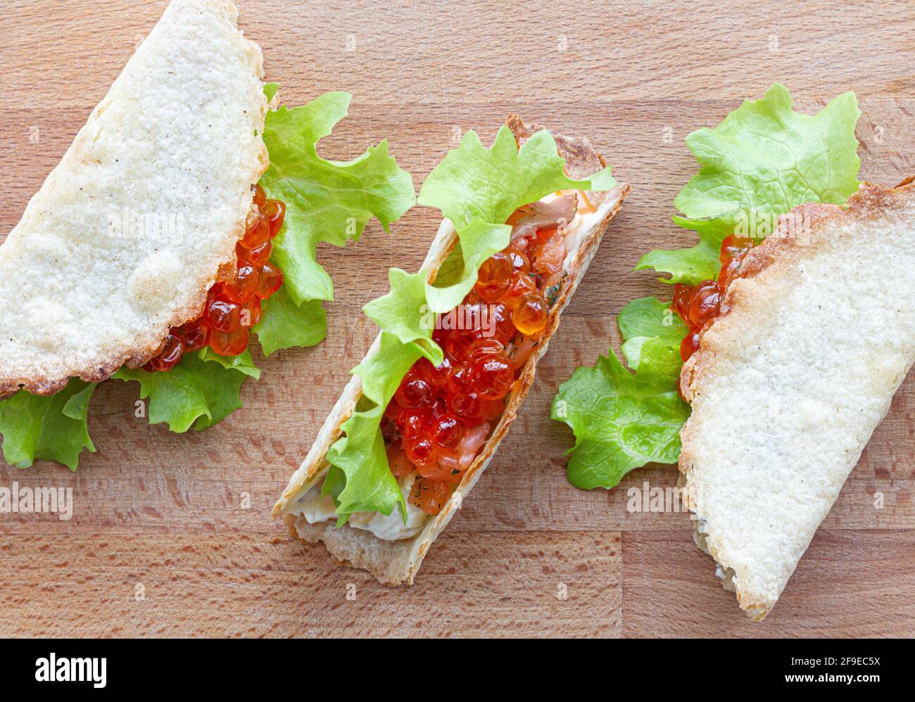 Kleine leckere Tacos mit rotem Kaviar und grünem Salat serviert Auf Holzschneidebrett auf Tisch Stockfoto