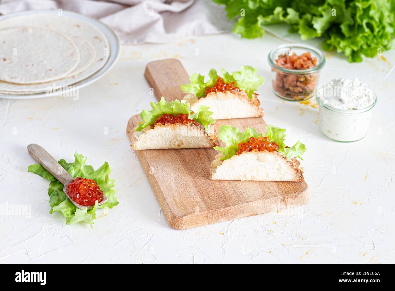 Kleine leckere Tacos mit rotem Kaviar und grünem Salat serviert Auf Holzschneidebrett auf Tisch Stockfoto