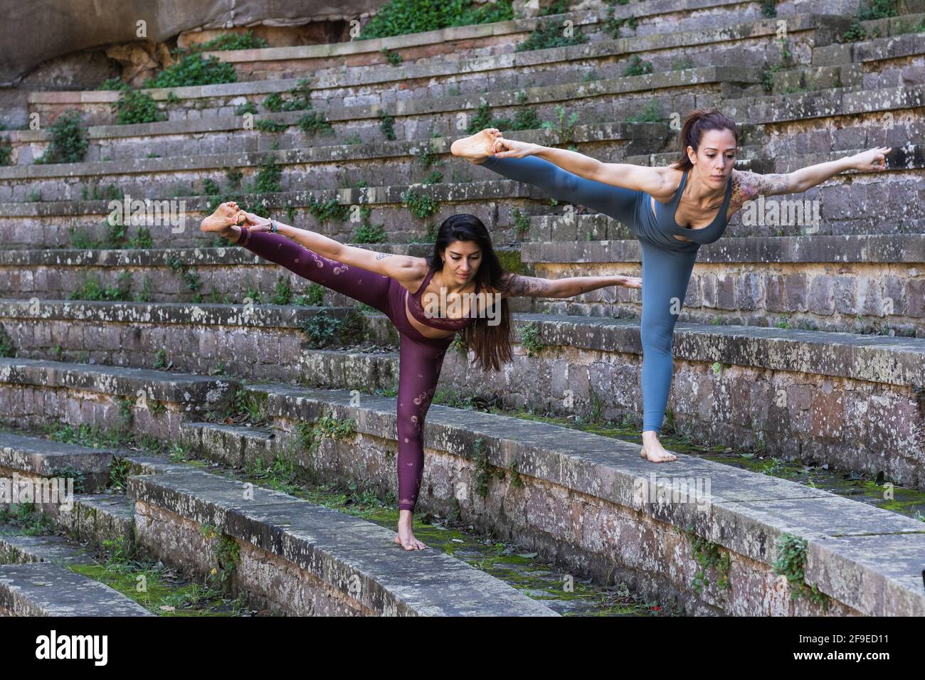 Flexible Weibchen im aktiven Balancieren in Hasta Padangusthasana im Stehen Auf Steintreppen und gemeinsam Yoga üben Stockfoto