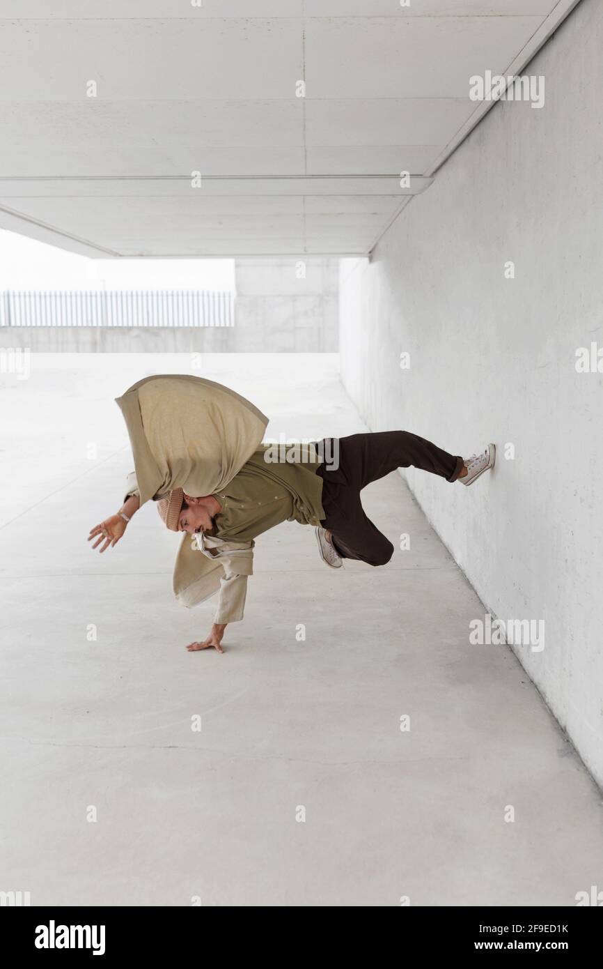 Männliche Tänzerin balanciert auf dem Arm und zeigt Breakdance-Bewegung während Lehnt sich an die Betonwand des Gebäudes in der Stadt Stockfoto