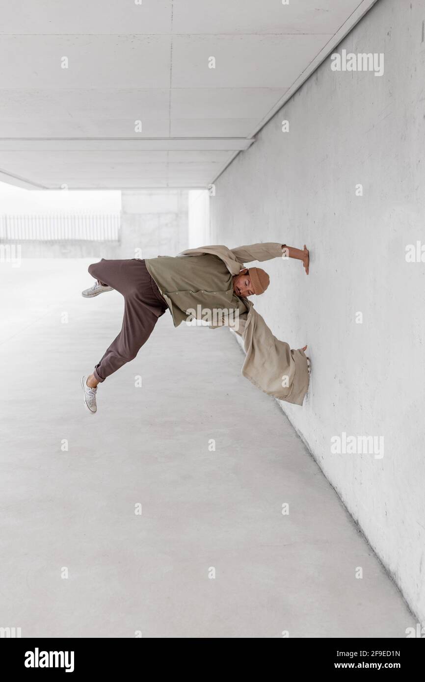 Männliche Tänzerin balanciert auf dem Arm und zeigt Breakdance-Bewegung während Lehnt sich an die Betonwand des Gebäudes in der Stadt Stockfoto