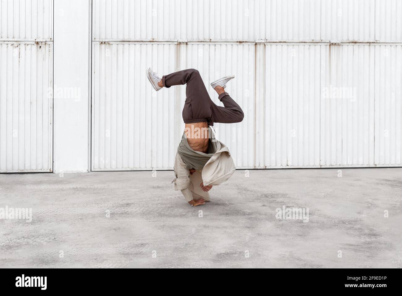 Nicht erkennbarer männlicher Tänzer, der Breakdance-Bewegungen zeigt, während er auf den Armen balanciert Und die Durchführung von Handhopps auf Betonboden im Stadtgebiet Stockfoto