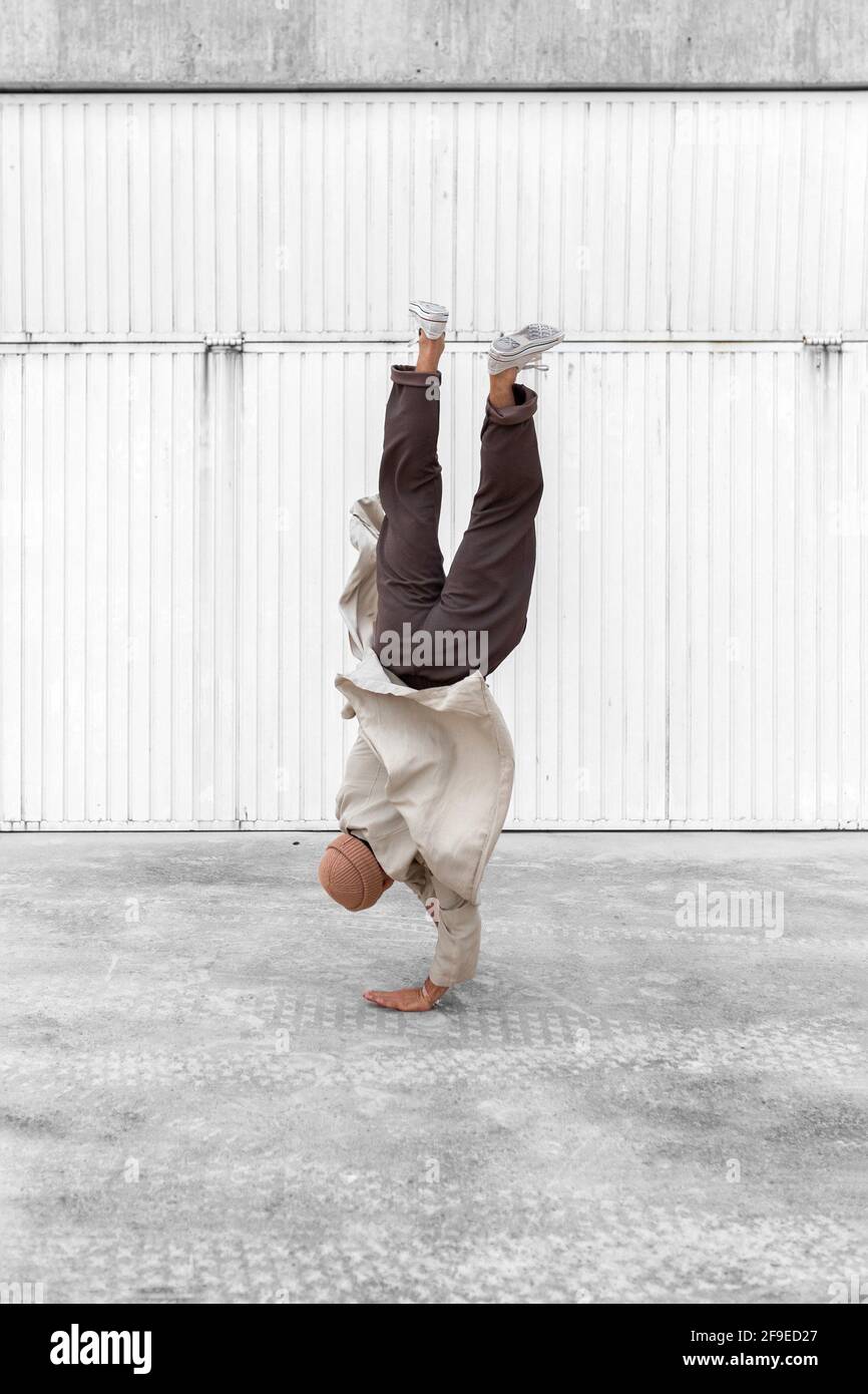 Nicht erkennbarer männlicher Tänzer, der Breakdance-Bewegungen zeigt, während er auf den Armen balanciert Und die Durchführung von Handhopps auf Betonboden im Stadtgebiet Stockfoto