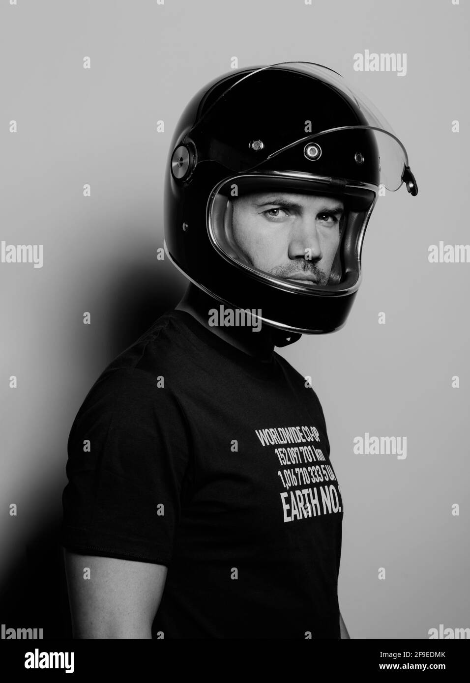 Seitenansicht eines selbstbewussten, brutalen erwachsenen Mannes in einem schwarzen Motorrad Der Helm blickt auf die Kamera, während er vor dem Hintergrund des Studios steht Stockfoto