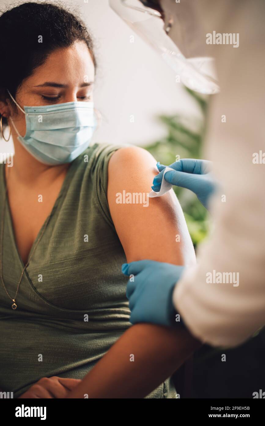 Frau, die zu Hause geimpft wird. Medizinisches Fachpersonal, das den Arm der Frau reinigt und desinfiziert, bevor es zu Hause eine Coronavirus-Impfung verabreicht. Stockfoto