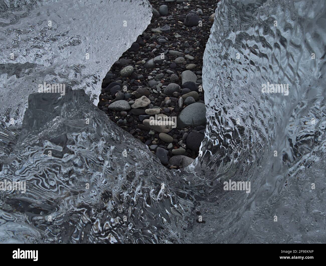 Nahaufnahme eines kleinen Eisbergs mit klarer, schimmernder Eisfläche am berühmten Diamond Beach in der Nähe der Gletscherlagune Jökulsárlón, Südisland mit Steinen. Stockfoto