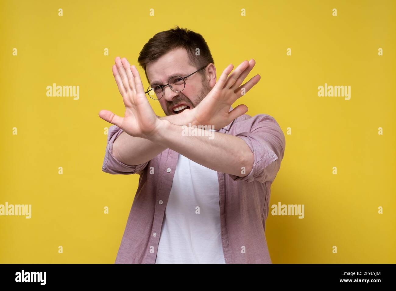 Kaukasischer Mann mit Brille und legerer Kleidung macht Stop-Geste, indem er gekreuzte Arme hebt und mit Ekel und Angst aussieht. Stockfoto